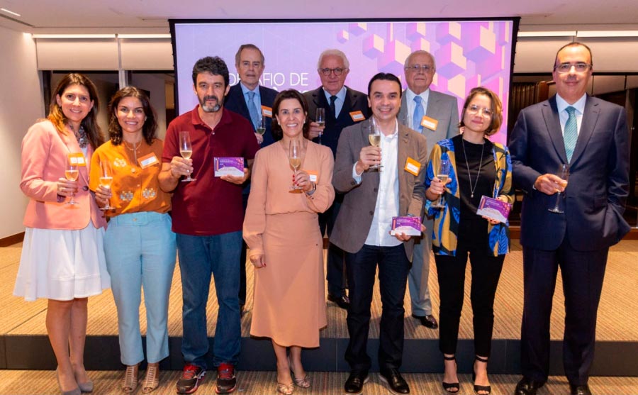 Foto em grupo de 10 pessoas, sendo quatro mulheres e seis homens. Eles posam lado a lado, sorrindo para a foto segurando taças de espumante. Três deles - dois homens e uma mulher - seguram uma placa de premiação cada um.